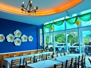 Een restaurant met blauwe wanden, witte bloemendecoraties en een bord met de tekst 'Welcome to our HOME'. Tafels zijn klaar voor het diner.