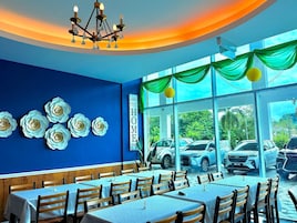 Un restaurante con paredes azules, adornos de flores blancas y un letrero que dice 'Welcome to our HOME'. Las mesas están dispuestas para comer.