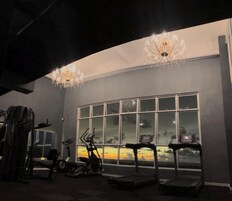 Un gimnasio con equipamiento de ejercicio, un amplio ventanal con vista al atardecer y candelabros.