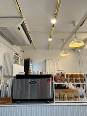 Eine gewerbliche Küche mit einer Edelstahl-Espressomaschine, einer Präsentation verpackter Waren und einem hellen Innenraum mit Deckenleuchten.
