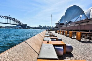 Eine Uferpromenade mit Sitzgelegenheiten, einer Brücke und einem modernen Opernhaus.