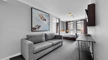 A modern living room with a grey sofa, a dining table, and a large abstract painting.