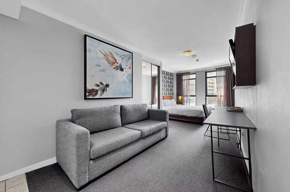A modern living room with a grey sofa, a dining table, and a large abstract painting. - KozyGuru | Sydney CBD | Refined Urban Retreat (Haymarket)