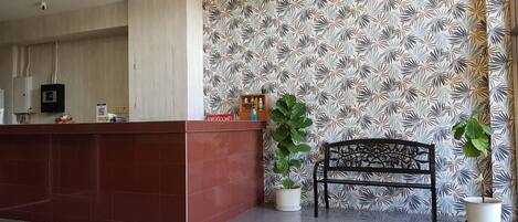 Un área de recepción con un mostrador rojo, un banco y dos plantas en macetas.