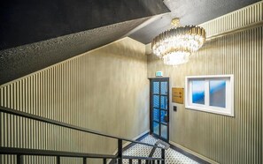 A staircase with a checkered floor leading to a lobby area with a chandelier, a door labeled "Lobby Parking," and a window with a view. - Urbannord (Seoul)