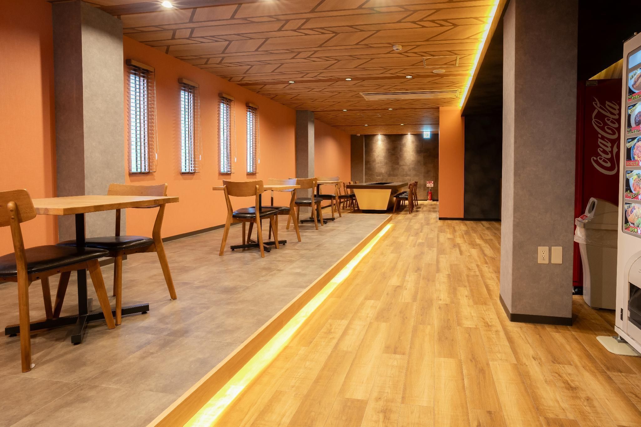 Un comedor moderno con mesas y sillas de madera, una barra larga y un refrigerador Coca-Cola.