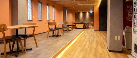 A modern dining area with wooden tables and chairs, a long counter, and a Coca-Cola refrigerator.