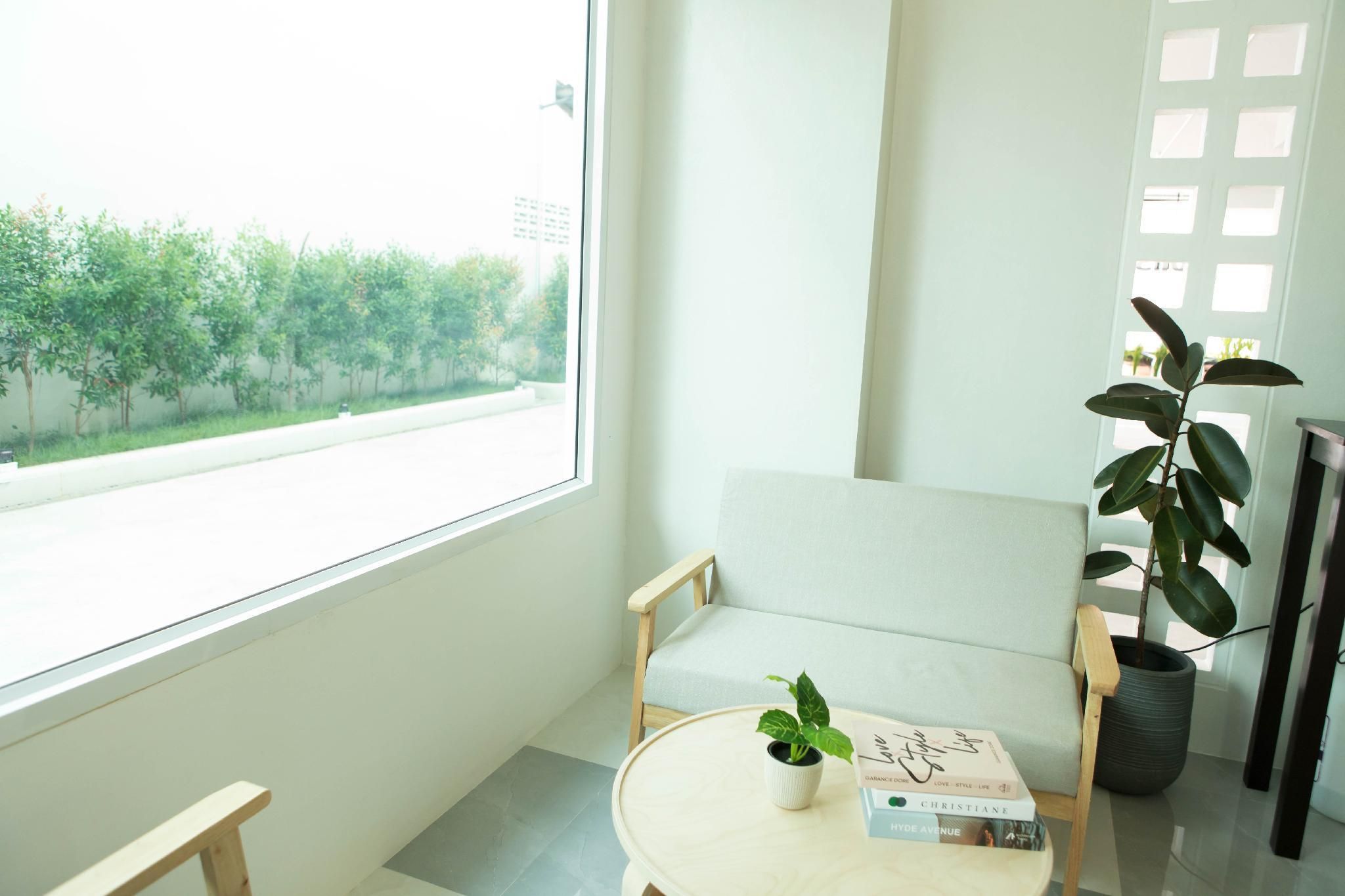 A room with a large window, a light-colored sofa, a small round table with a potted plant and a book, and a tall potted plant beside the sofa.