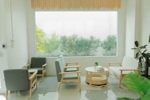 A modern living room with a large window, two grey chairs, a white sofa, and a round wooden table. - S1 Trang Hotel (Trang)