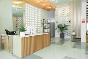 A reception area with a wooden reception desk, a glass partition, and a wall with circular patterns. - S1 Trang Hotel (Trang)