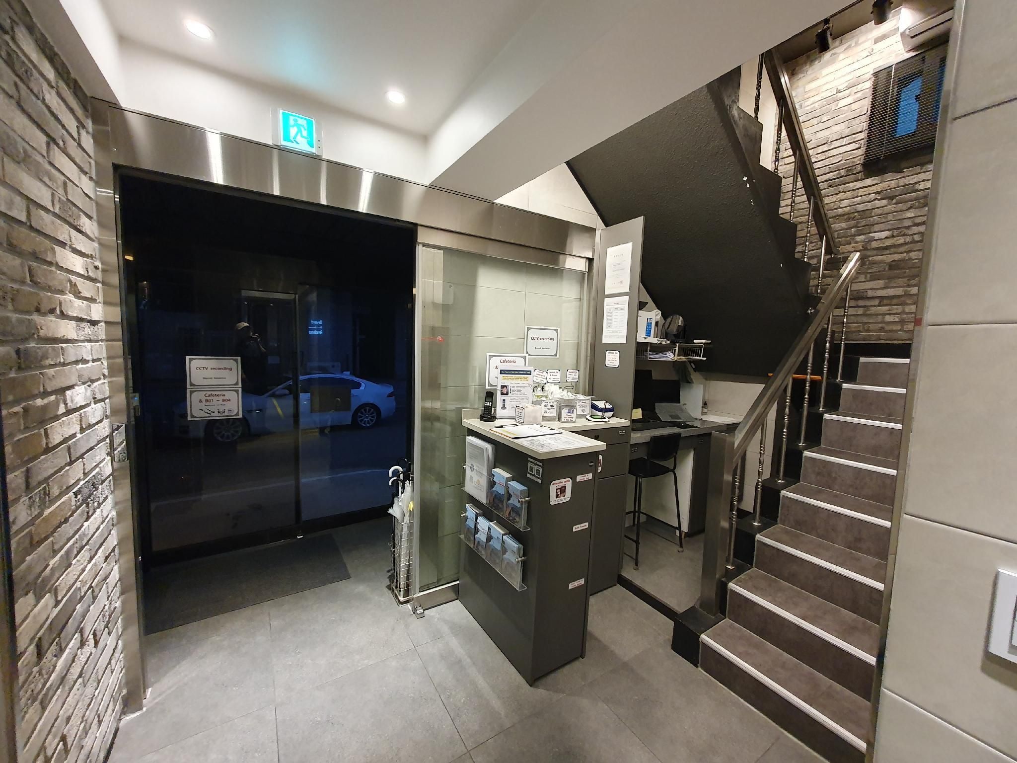 A modern hotel lobby with a glass door entrance, a staircase, and a reception desk.