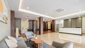 A modern hotel lobby with a reception desk, seating area, and a reception counter. - Kio Hotel Korat (Nakhon Ratchasima)