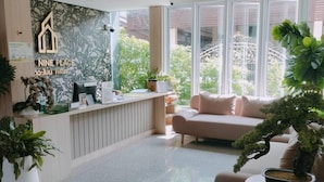 A modern reception area with a wooden reception desk, a large potted plant, a sofa, and a ceiling fan.