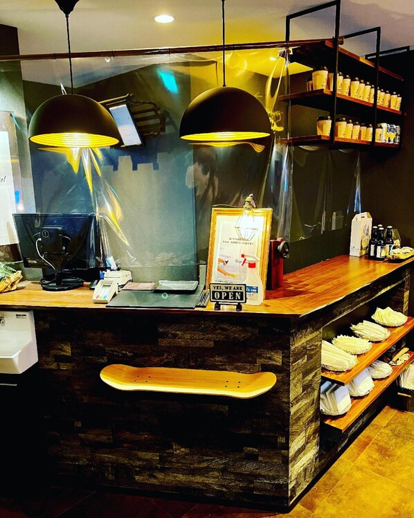 A counter with a sign indicating the establishment is open, a cash register, a phone, and a wooden bench. - Enoca Hotel (Fujisawa)