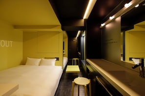Une chambre d’hôtel avec un lit, un petit tabouret, un miroir et un mur sur lequel est affiché un panneau.