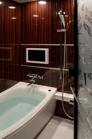 Une salle de bain moderne avec une baignoire sur pieds, une douchette et un téléviseur fixé au mur.