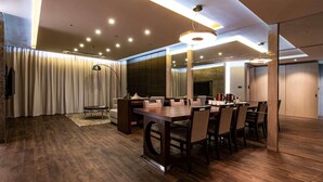 A modern conference room with a wooden table and chairs, recessed ceiling lighting, and a large window with curtains. - Ramada Suites Geoje (Pyeongtaek)