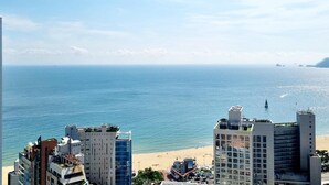 A coastal cityscape with a beach, a lighthouse, and several high-rise buildings including a hotel.