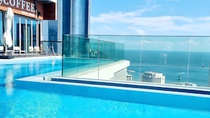 A modern infinity pool with a glass barrier, overlooking a cityscape and the ocean.