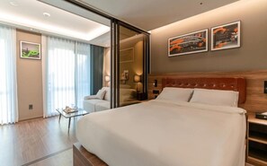 Ein modernes Hotelzimmer mit einem großen Bett, einem Glastisch, einer Couch und Blick auf die Stadt durch das Fenster.