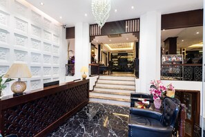 A lobby with a reception desk, a staircase leading to a bar area, and a seating area with a vase of flowers. - Hanoi Memory Premier Hotel Spa (Hanoi)
