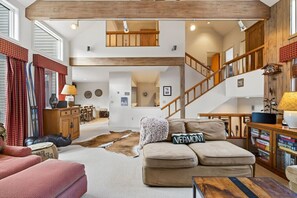A spacious living room with a high ceiling, a staircase, and a cozy fireplace. - Spacious Piper Ridge Townhome Near Stratton (Winhall)