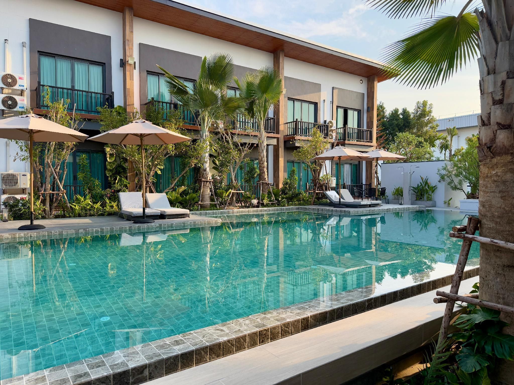 Piscina com espreguiçadeiras e guarda-sóis, cercada por vegetação e um edifício moderno com sacadas.
