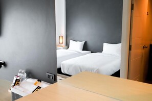 Une chambre d’hôtel avec deux lits, une table de chevet avec des articles de toilette, une lampe et une porte.