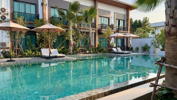 A swimming pool with lounge chairs and umbrellas, surrounded by greenery and a modern building with balconies. - The Rest Hotel - Prachuab Kriri Khan (Prachuap Khiri Khan)