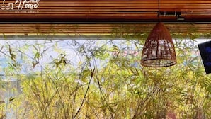 Una habitación con un sofá, dos sillones de mimbre, una mesita redonda con un jarrón de flores rojas y una lámpara colgante.
