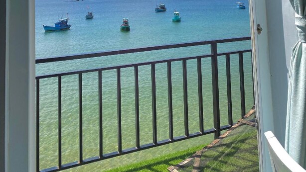 Un balcón con vistas despejadas al mar, varios barcos y una costa lejana.