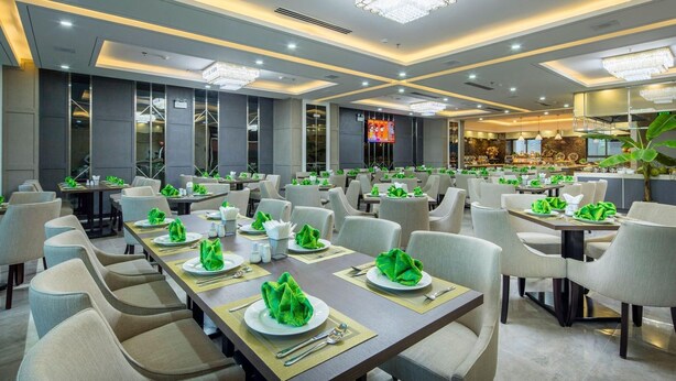 A spacious dining area with multiple tables set for guests, featuring modern chandeliers and a bar area in the background. - B&n Hotel (Nha Trang)