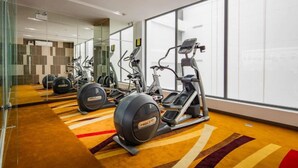 A modern gym with cardio equipment, a mirrored wall, and a patterned carpet. - B&n Hotel (Nha Trang)