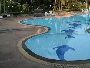 Piscina con murales de delfines, sillas de descanso y un muro de piedra.