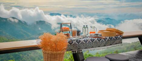 A table set with food and drinks, overlooking a mountainous landscape.