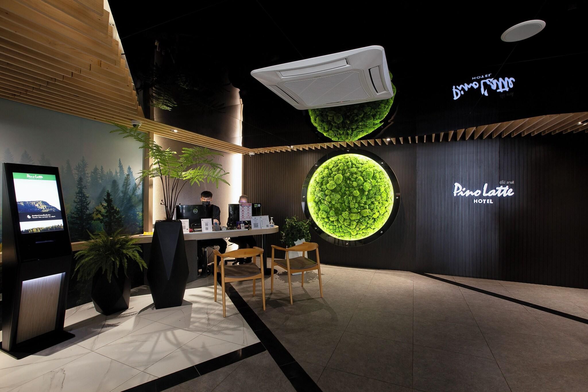 A reception area with a digital kiosk, a reception desk, two wooden chairs, and a large illuminated green wall.
