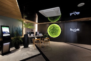 A reception area with a digital kiosk, a reception desk, two wooden chairs, and a large illuminated green wall. - Pino Latte Resort And Hotel (Khao Kho)