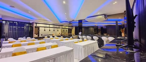 A conference room with rows of tables, white tablecloths, and yellow sashes.