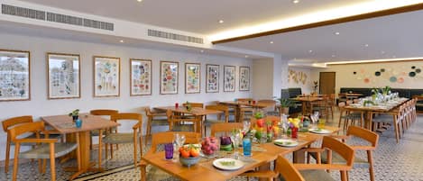 A spacious dining area with multiple tables and chairs, framed botanical artwork on the walls, and a patterned floor.