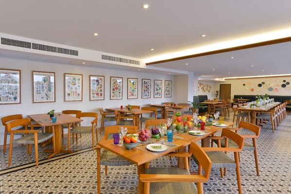 A spacious dining area with multiple tables and chairs, framed botanical artwork on the walls, and a patterned floor. - The Raintree Hotel (Chiang Mai)