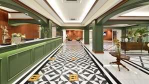 Un vestíbulo de hotel con piso de diseño geométrico, paneles verdes y una recepción decorada con objetos ornamentales.