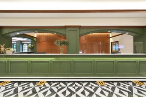 A reception area with a green reception desk, a patterned floor, and a wooden wall with vertical slats. - The Raintree Hotel (Chiang Mai)