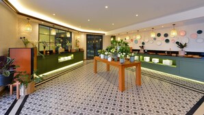 Un moderno vestíbulo de hotel con un mostrador de recepción curvo, una mesa de madera central con plantas en macetas y un suelo con diseño.
