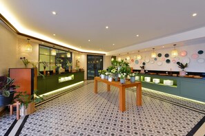 A modern hotel lobby with a curved reception desk, a central wooden table with potted plants, and a patterned floor. - The Raintree Hotel (Chiang Mai)
