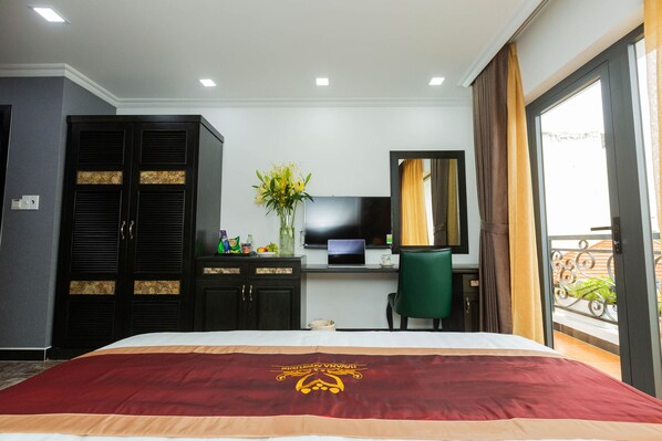 Une chambre d’hôtel avec un lit, un bureau avec un ordinateur, une chaise, une télévision et une fenêtre avec des rideaux.