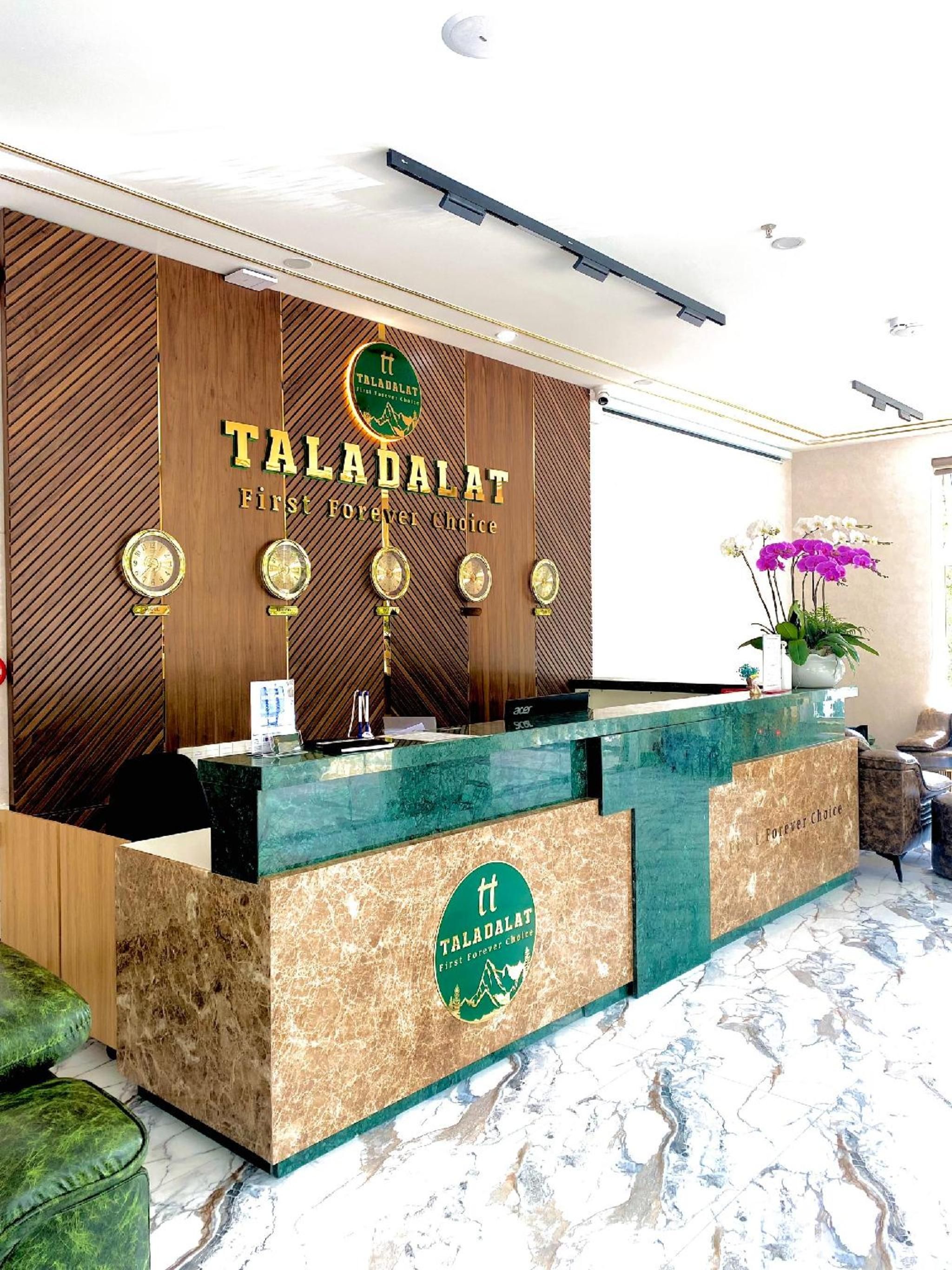 A reception desk with 'TALADALAT' branding, a wooden panel wall, and a marble floor.
