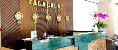 A reception desk with 'TALADALAT' branding, a wooden panel wall, and a marble floor.