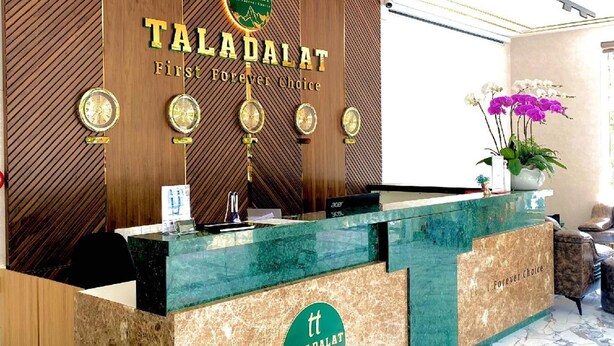 Un comptoir d’accueil arborant le logo « TALADALAT », un mur recouvert de panneaux en bois et un sol en marbre.