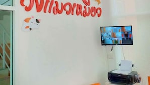 A reception area with a large wall sign, a flat-screen TV mounted on the wall, and a printer on a stand. - Wangmaewmeo (Rayong)