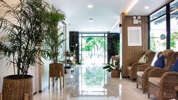 A hotel lobby with a polished floor, wicker furniture, and potted plants.